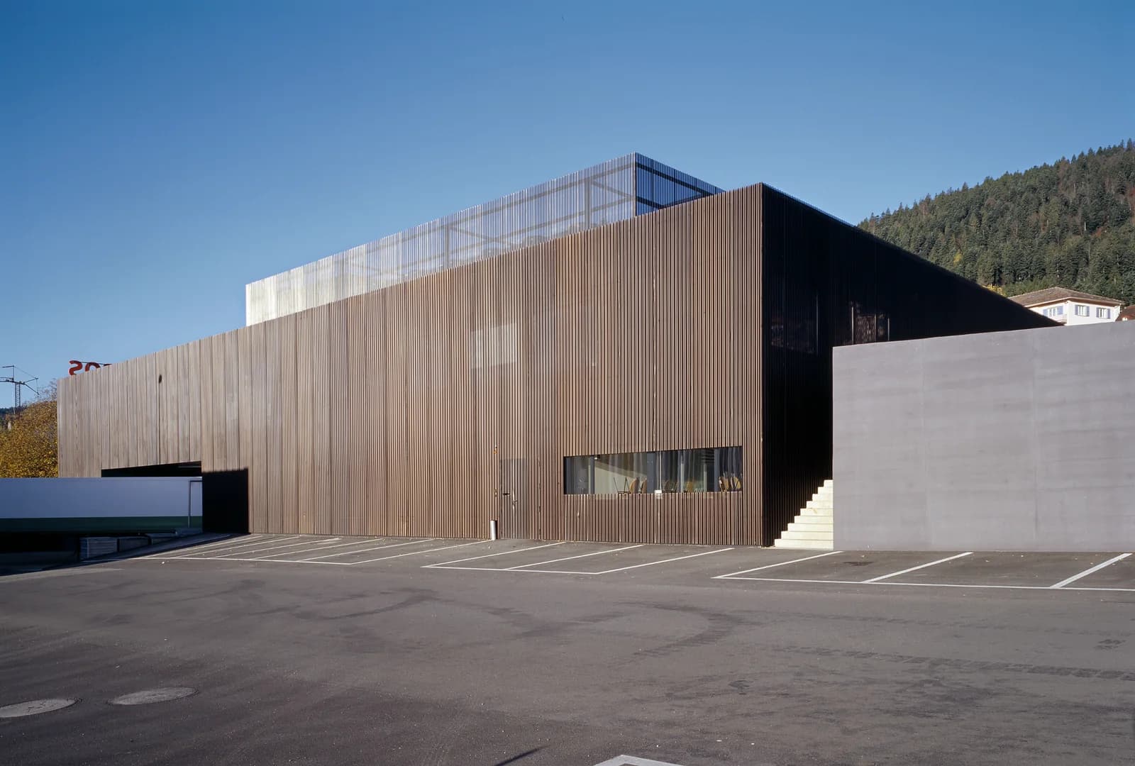 Commercial building with bronze cladding beside a wooded hill