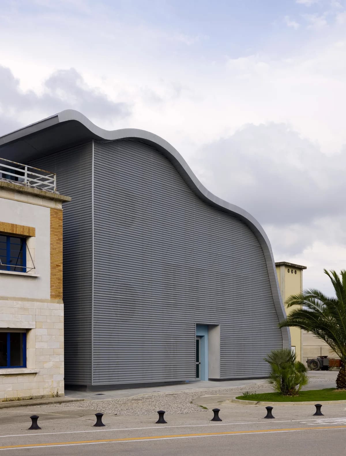 Wave-shaped metal façade beside a stone building